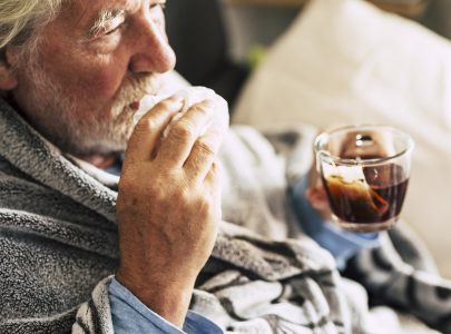 One old senior man with cold flu influenza symptoms drinking medicine or natural herbal tea at home to heal. Concept of virus and mature elderly people with health problems. People and winter diseases