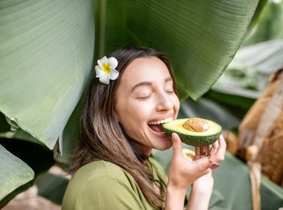 Young woman eating avocado berry in the banana leaves outdoors. Concept of vegetarianism, healthy eating and wellbeing