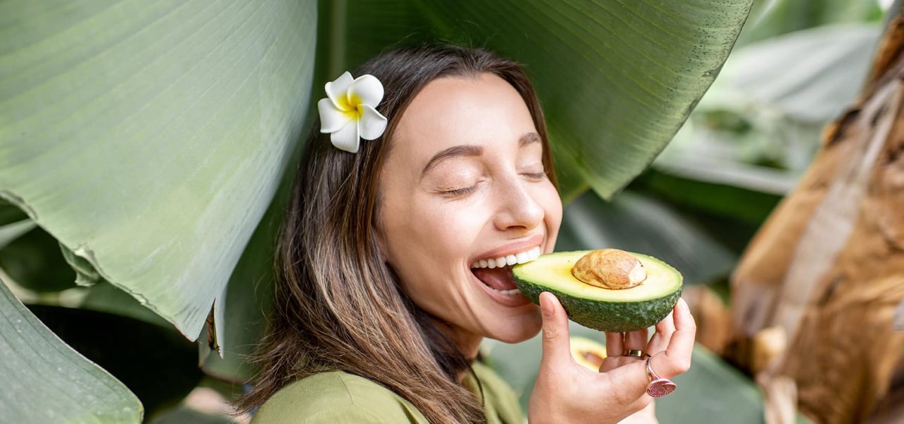 Young woman eating avocado berry in the banana leaves outdoors. Concept of vegetarianism, healthy eating and wellbeing