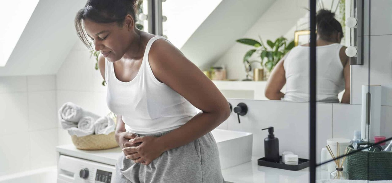 Young African-American woman standing in the bathroom and feeling pain in the stomach