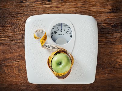 Green apple wrapped in a tape measure on a white scale, wooden surface on background, dieting and weight loss concept