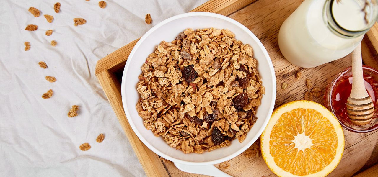 Good morning. Breakfast on white bed sheets. Muesli or granola, milk, orange  on wooden tray from above. Top view.  Flat lay. Copy space. Hotel Room Early Morning.