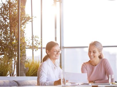 Cheerful attractive young businesswomen sitting at table in modern cafe and viewing survey results while creating advertising plan for new product