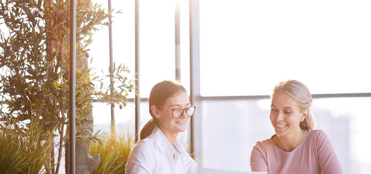 Cheerful attractive young businesswomen sitting at table in modern cafe and viewing survey results while creating advertising plan for new product